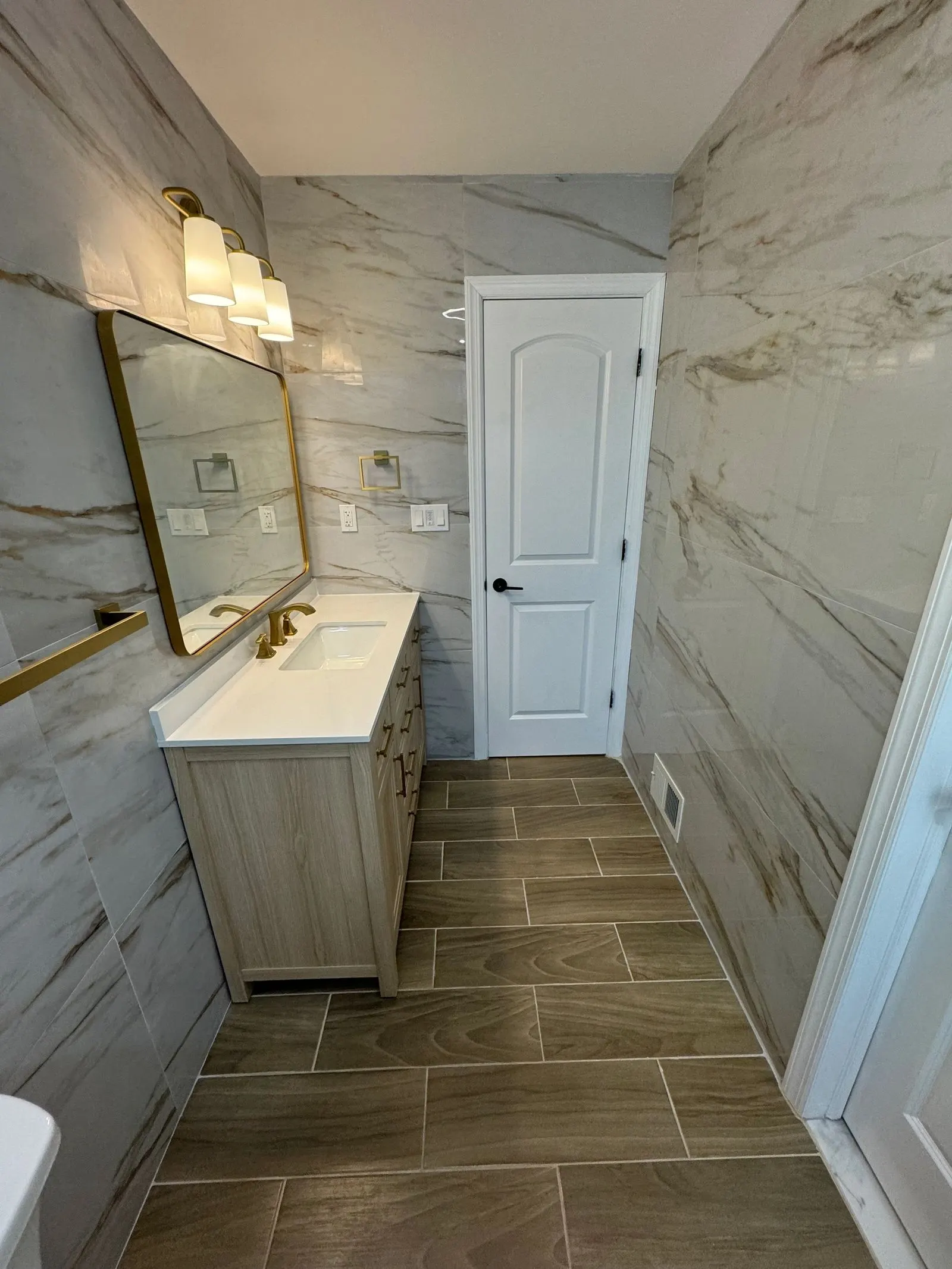 Vanity with brushed gold fixtures against large veined wall tile